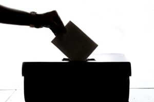 Immagine stilizzata di una mano che inserisce tessera elettori in una urna